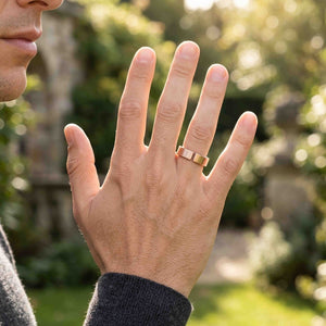 8 of 10: Close view of a man wearing a handmade 6mm matte bronze cuff ring outdoors, with his hand raised in natural light and a softly blurred garden in the background.