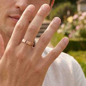 4 of 10: Close view of a man wearing a handmade 6mm matte bronze cuff ring outdoors, with his hand raised near his face and a softly blurred garden in the background.
