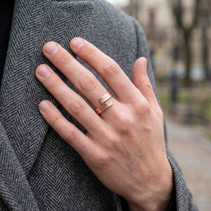 2 of 9: Close view of a man's hand wearing the 5.5mm bark copper bypass ring against a gray herringbone wool coat, showing the warm copper color, open wrap shape, and hand applied bark texture in an urban outdoor setting.