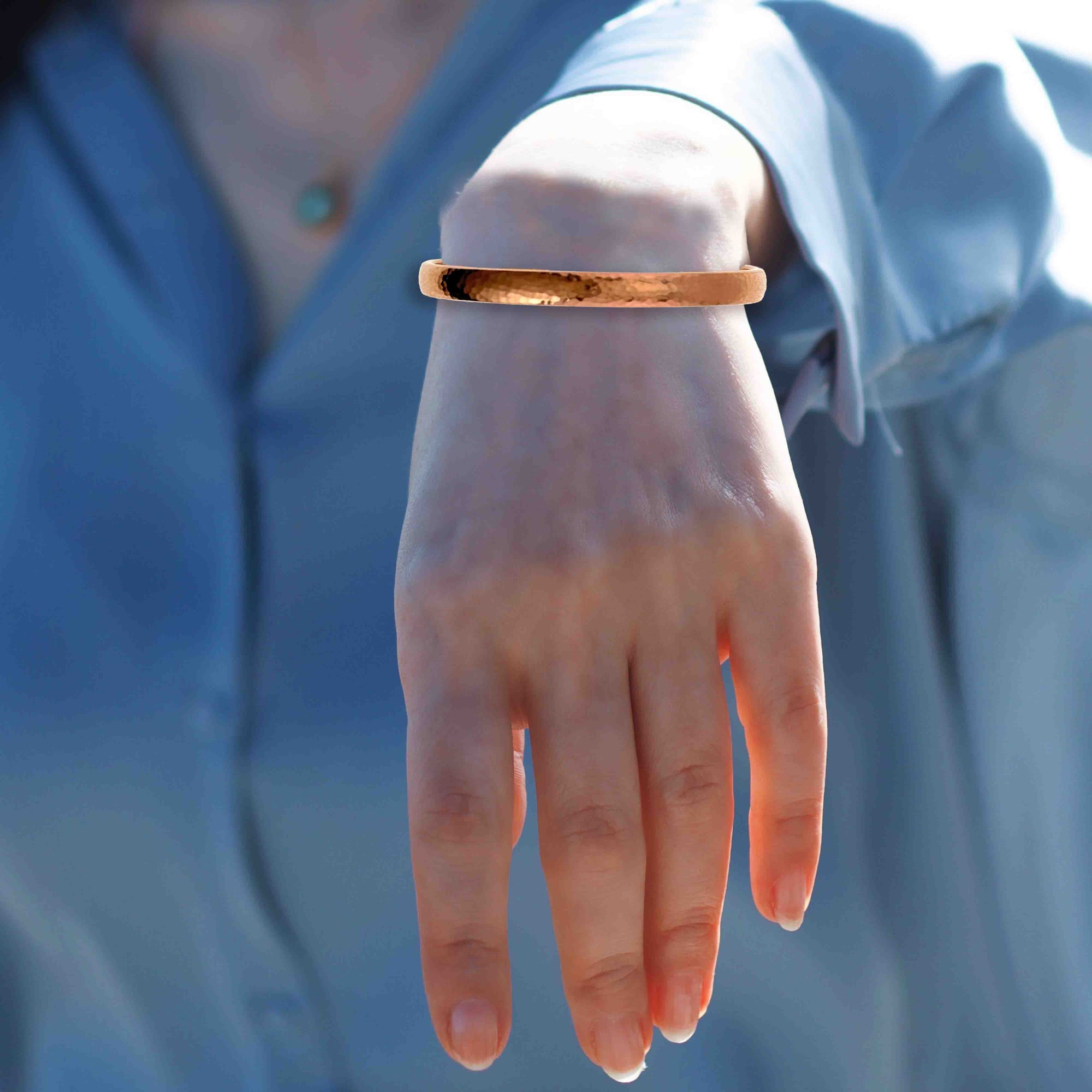 A woman's wrist wearing a 7mm Domed Hammered Copper Cuff Bracelet with a blurred blue background