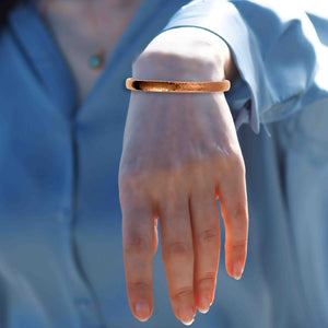 4 of 9: A woman's wrist wearing a 7mm Domed Hammered Copper Cuff Bracelet with a blurred blue background