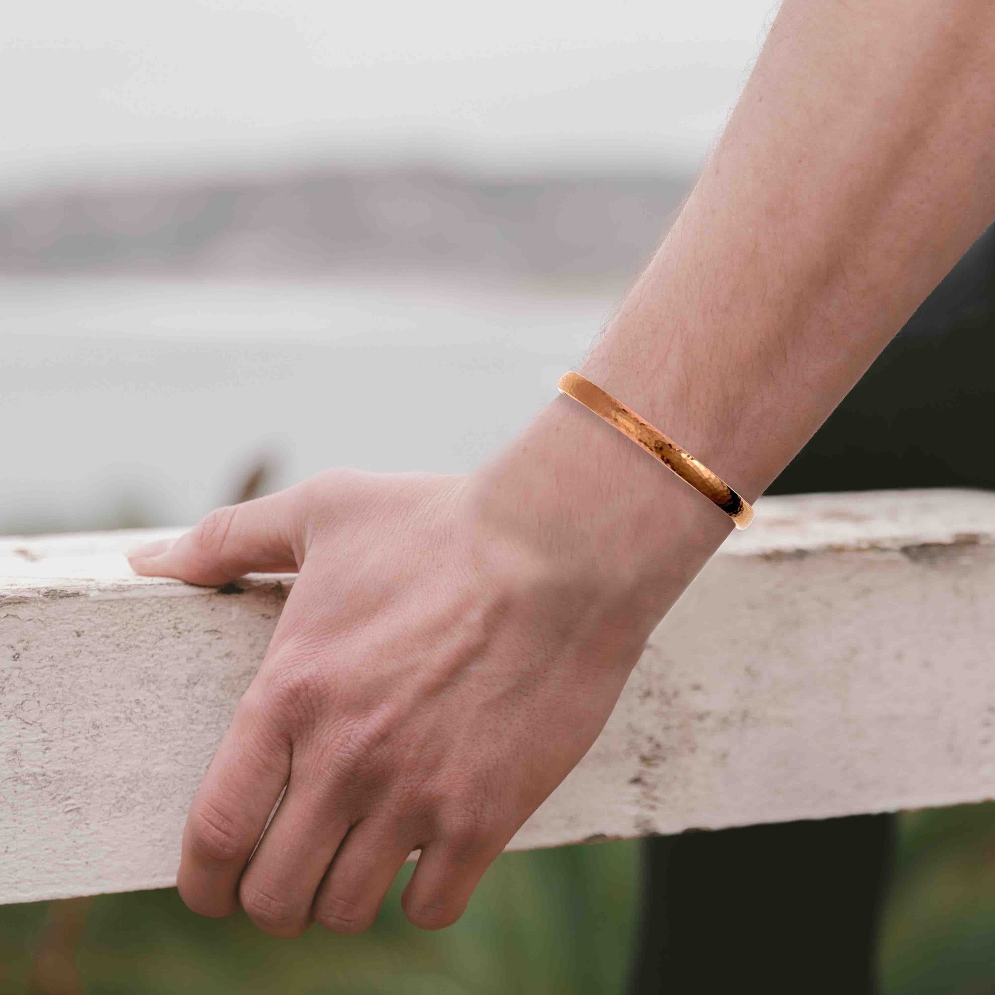 A Man's arm wearing a 7mm Domed Hammered Copper Cuff Bracelet on a blurred natural background