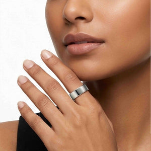 4 of 9: Polished stainless steel flat band ring worn on a woman’s finger near her face, featuring a wide 7mm profile, smooth reflective silver finish, flat surface, and modern unisex style against a soft white background.