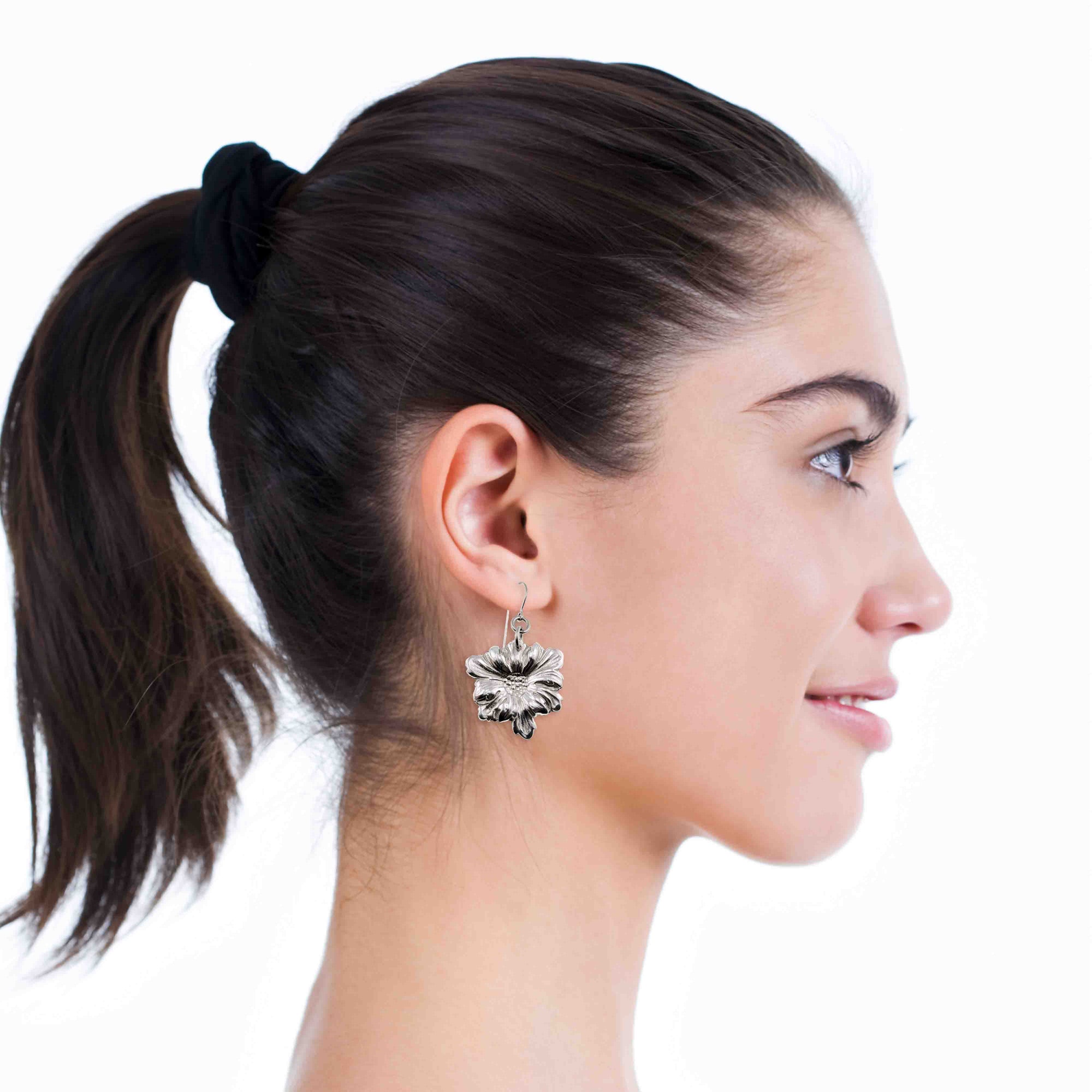 Close-up of a woman wearing Dogwood Blossom Aluminum Drop Earrings with a plain background