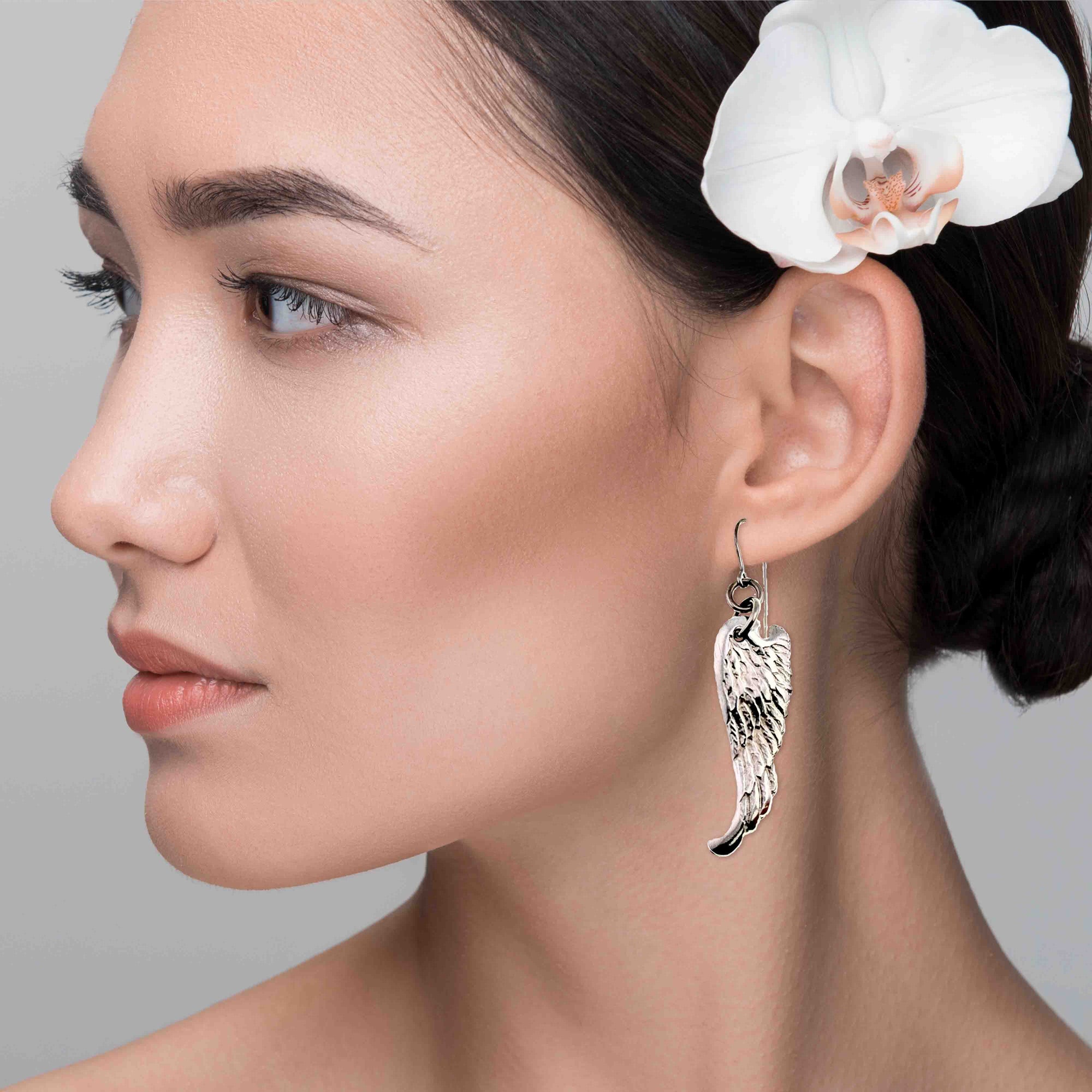 Close-up of a woman wearing Aluminum Guardian Angel Wing Drop Earrings with a white orchid in her hair.