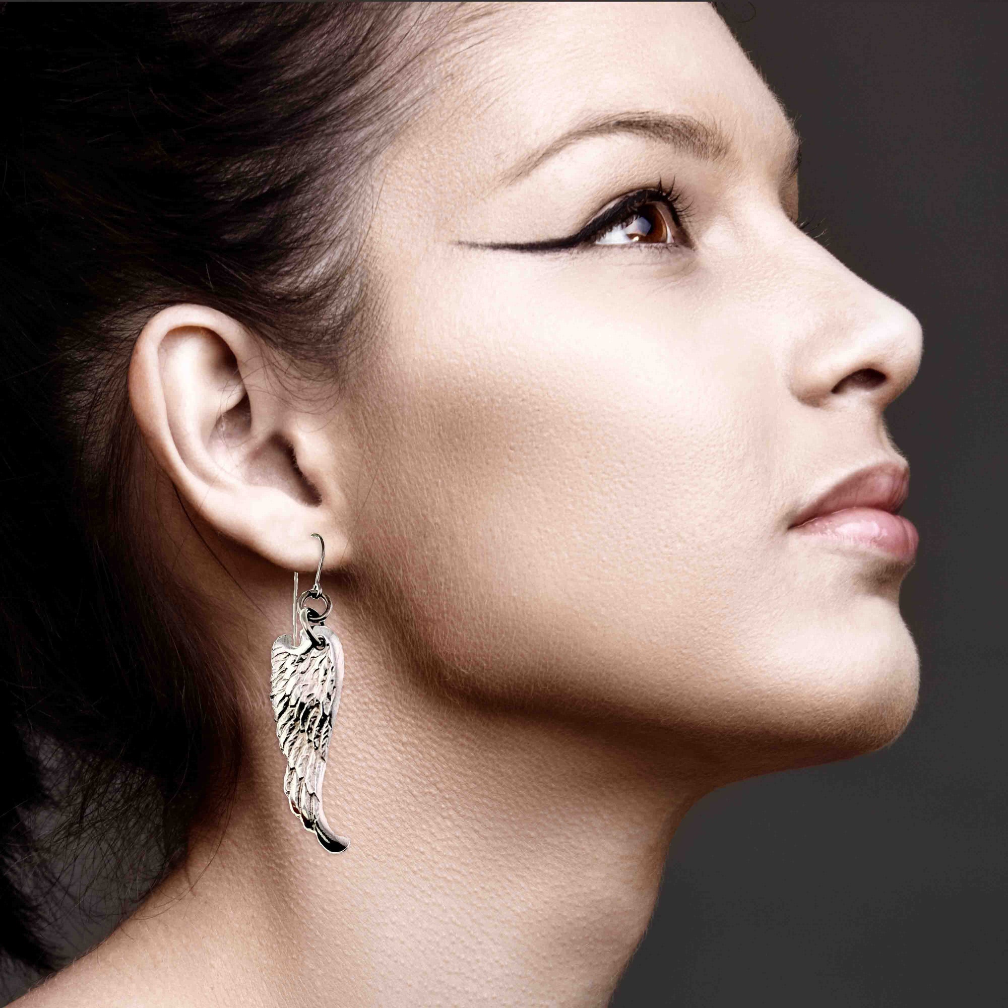 Close-up of a woman wearing Aluminum Guardian Angel Wing Drop Earrings with a dark background