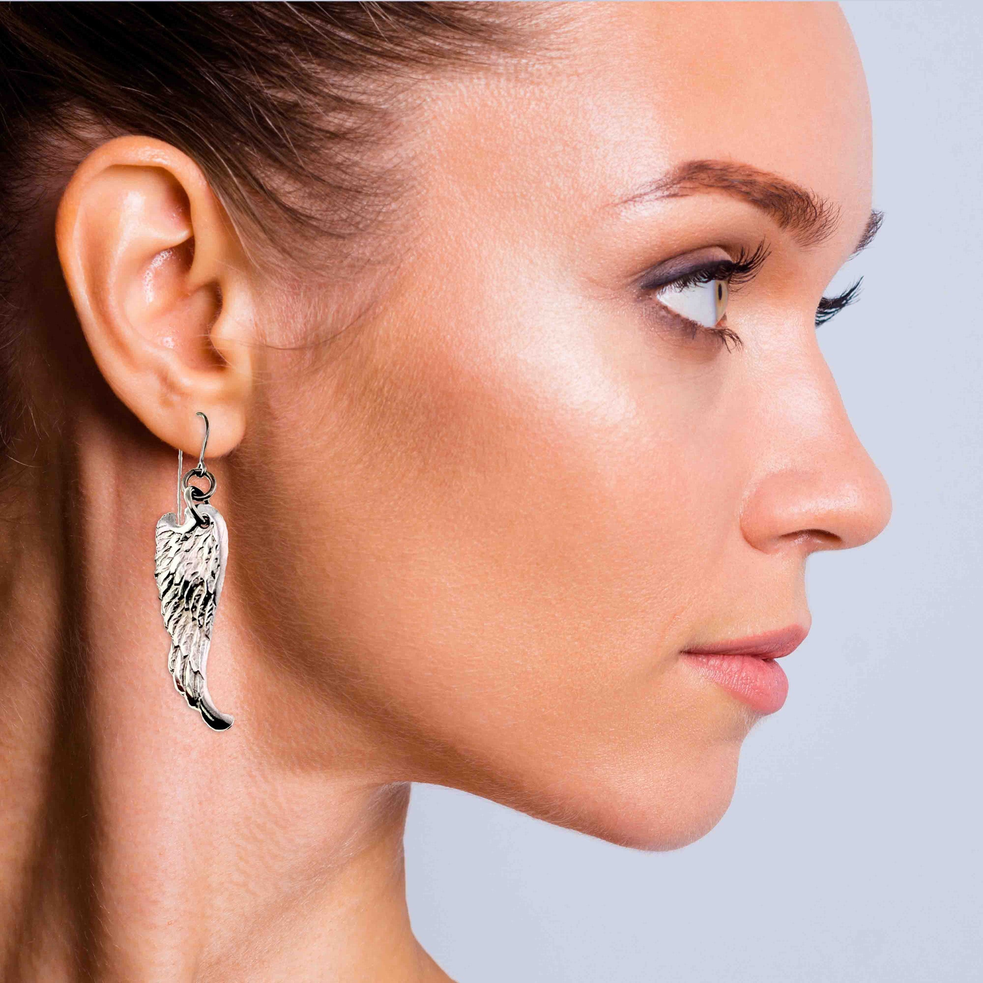 Close-up of a woman wearing Aluminum Guardian Angel Wing Drop Earrings against a neutral background