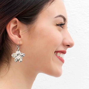 4 of 7: A Smiling Woman Wearing Aluminum Hibiscus Flower Dangle Earrings