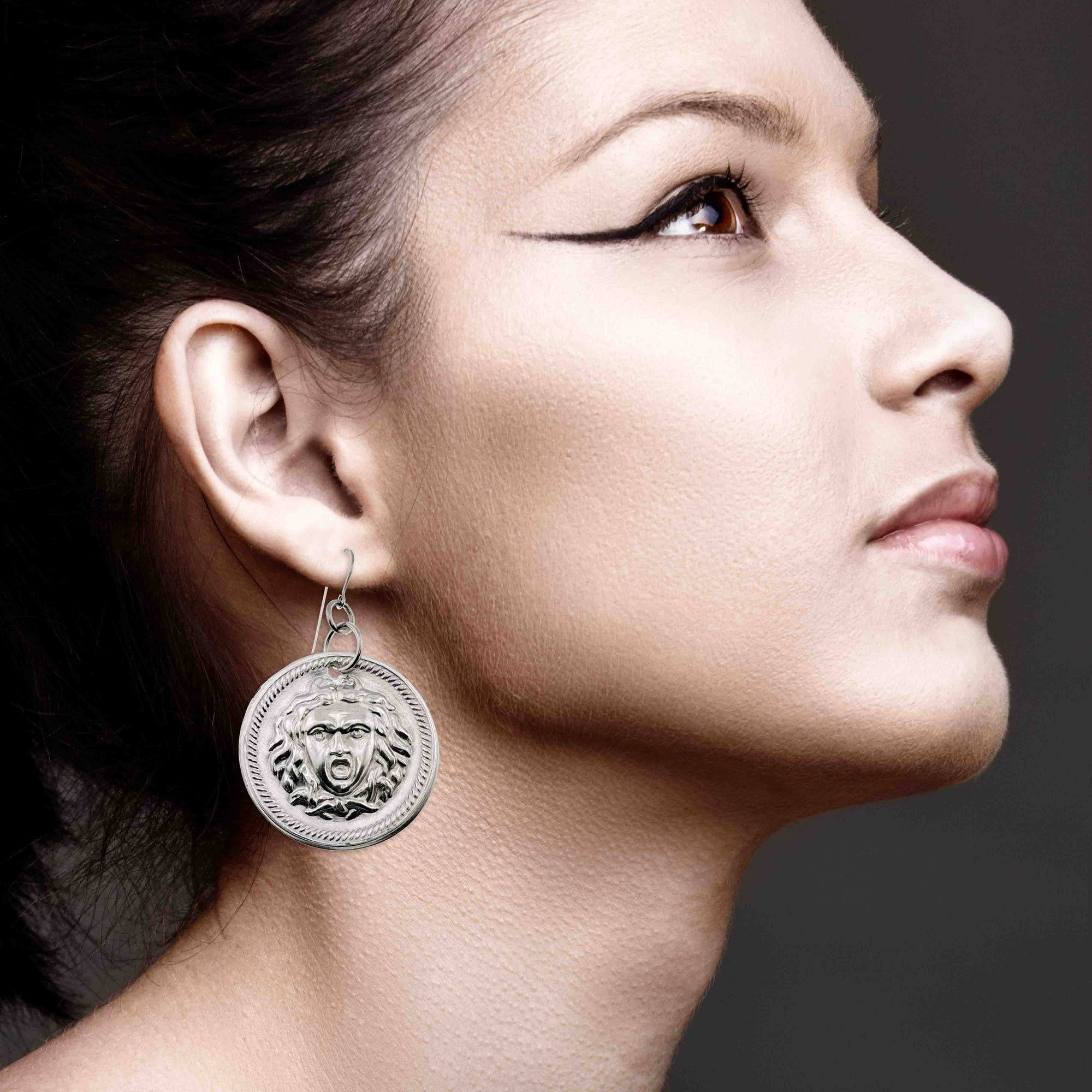 Close-up of a woman wearing Aluminum Medusa Disc Drop Earrings with a dark background