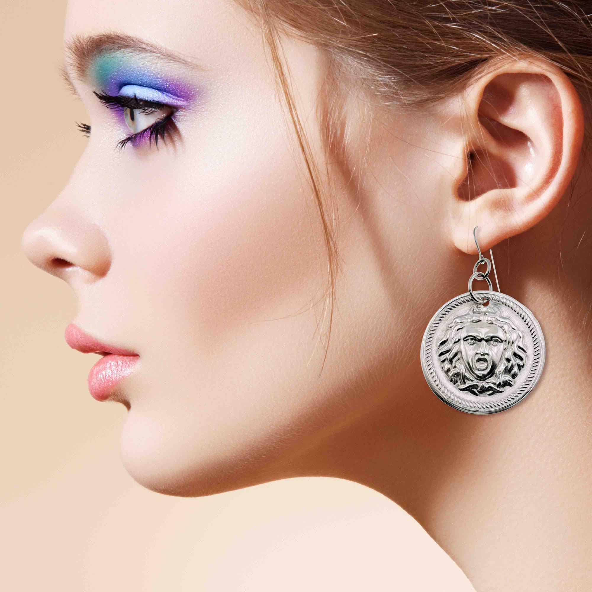 Close-up of a woman's profile wearing Aluminum Medusa Disc Drop Earrings against a beige background