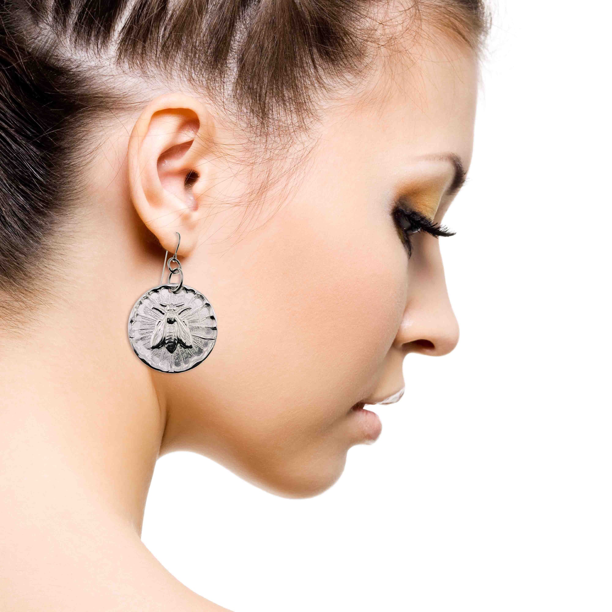 Close-up of a woman wearing Aluminum Queen Bee Disc Drop Earrings  with a white background