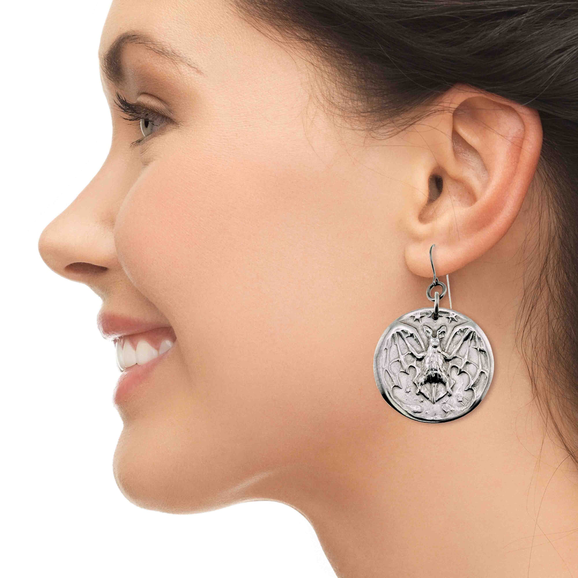 Close-up of a woman wearing Aluminum Vampire Bat Disc Dangle Earrings with intricate design