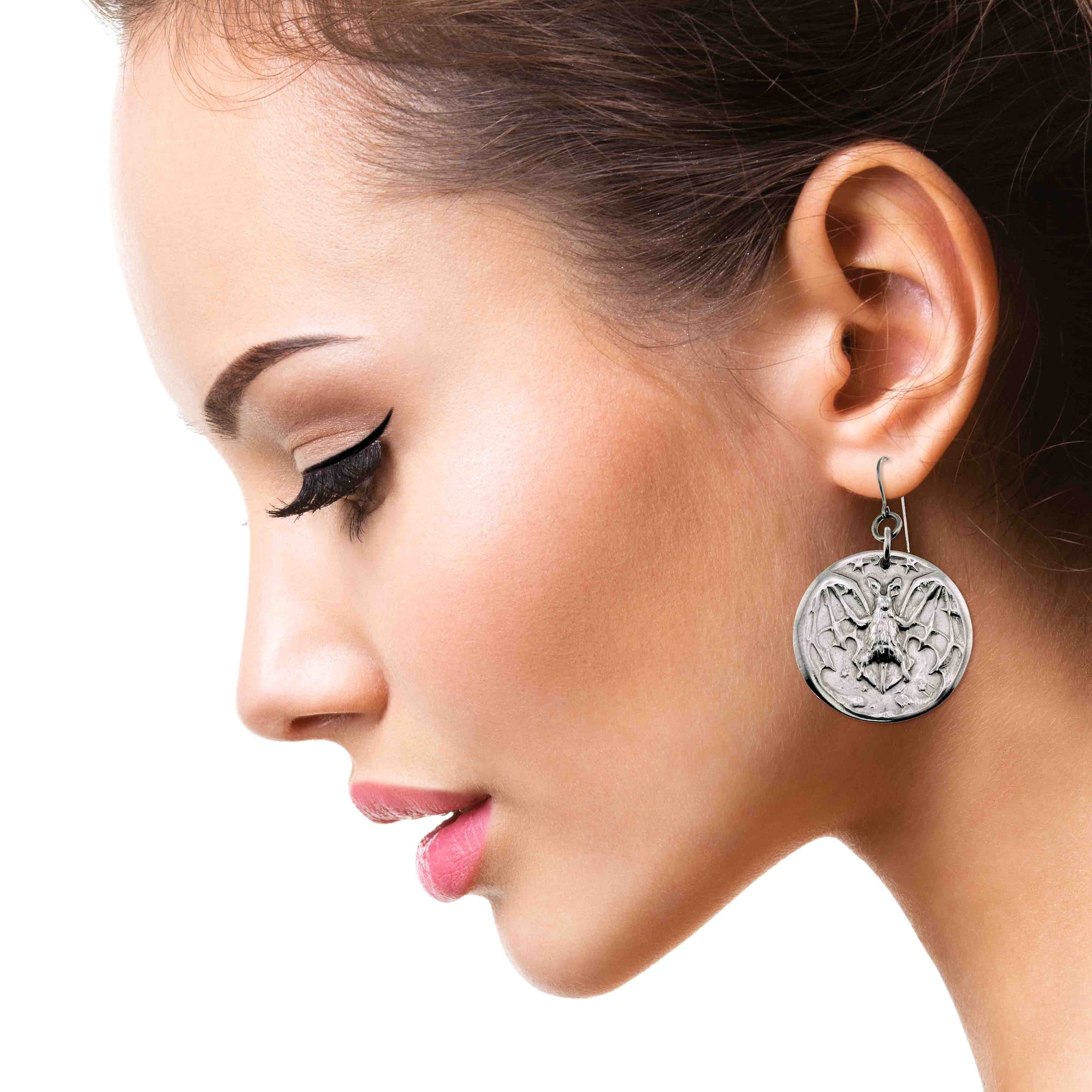 Close-up of a woman wearing Aluminum Vampire Bat Disc Dangle Earrings with a detailed design.
