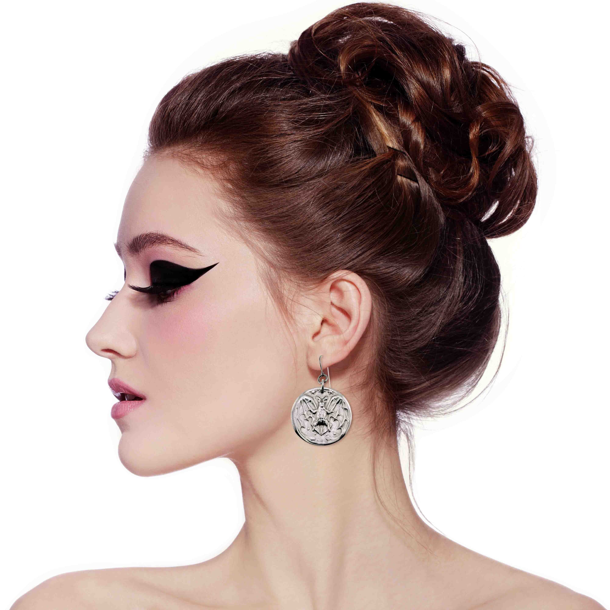 Woman with stylish hair and makeup on a white background wearing Aluminum Vampire Bat Disc Dangle Earrings