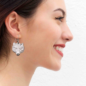 6 of 7: A Smiling Woman Wearing Aluminum Wolf Head Earrings