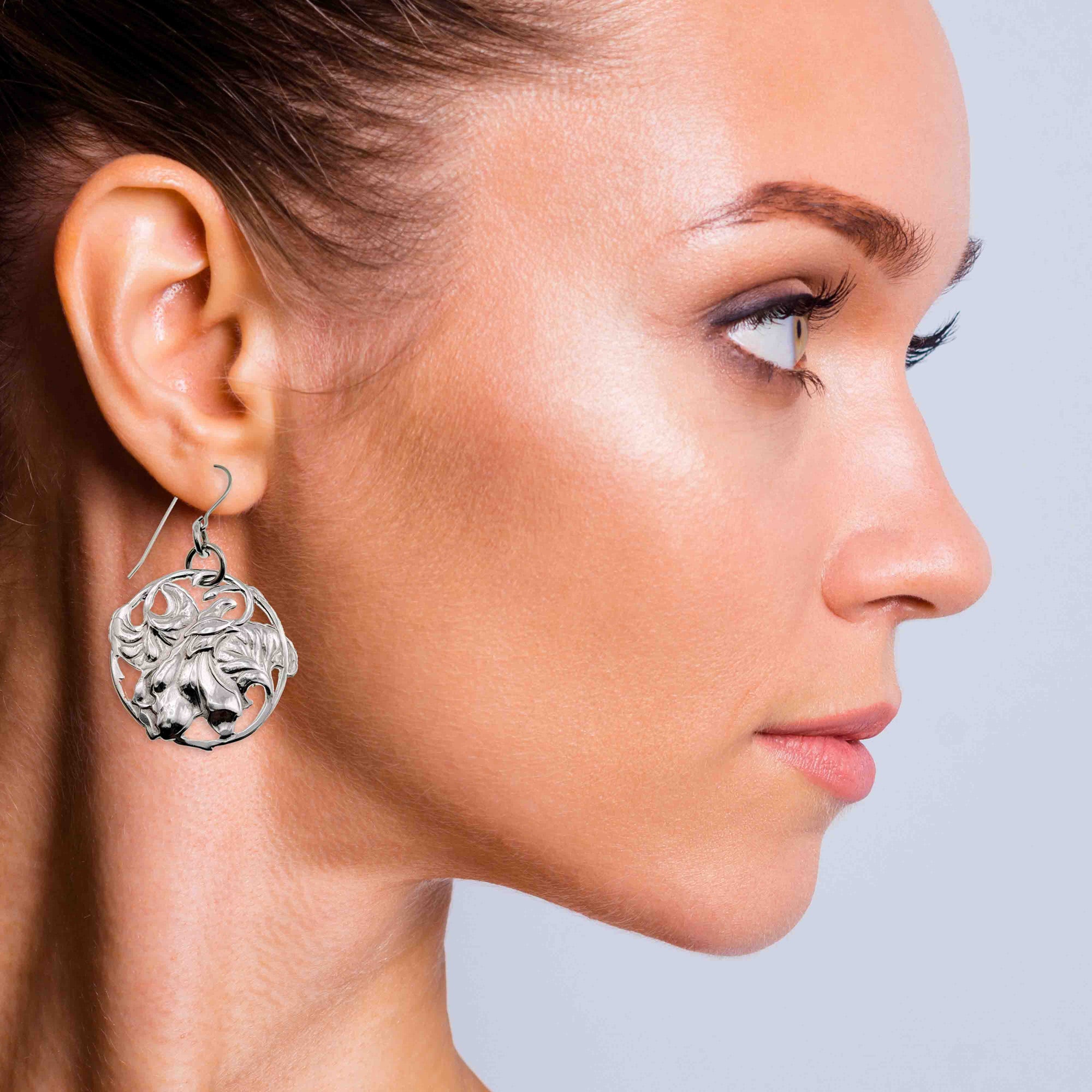 Close-up of a woman wearing a silver earring with Art Nouveau Aluminum Lily Flower Disc Drop Earrings on a light gray background