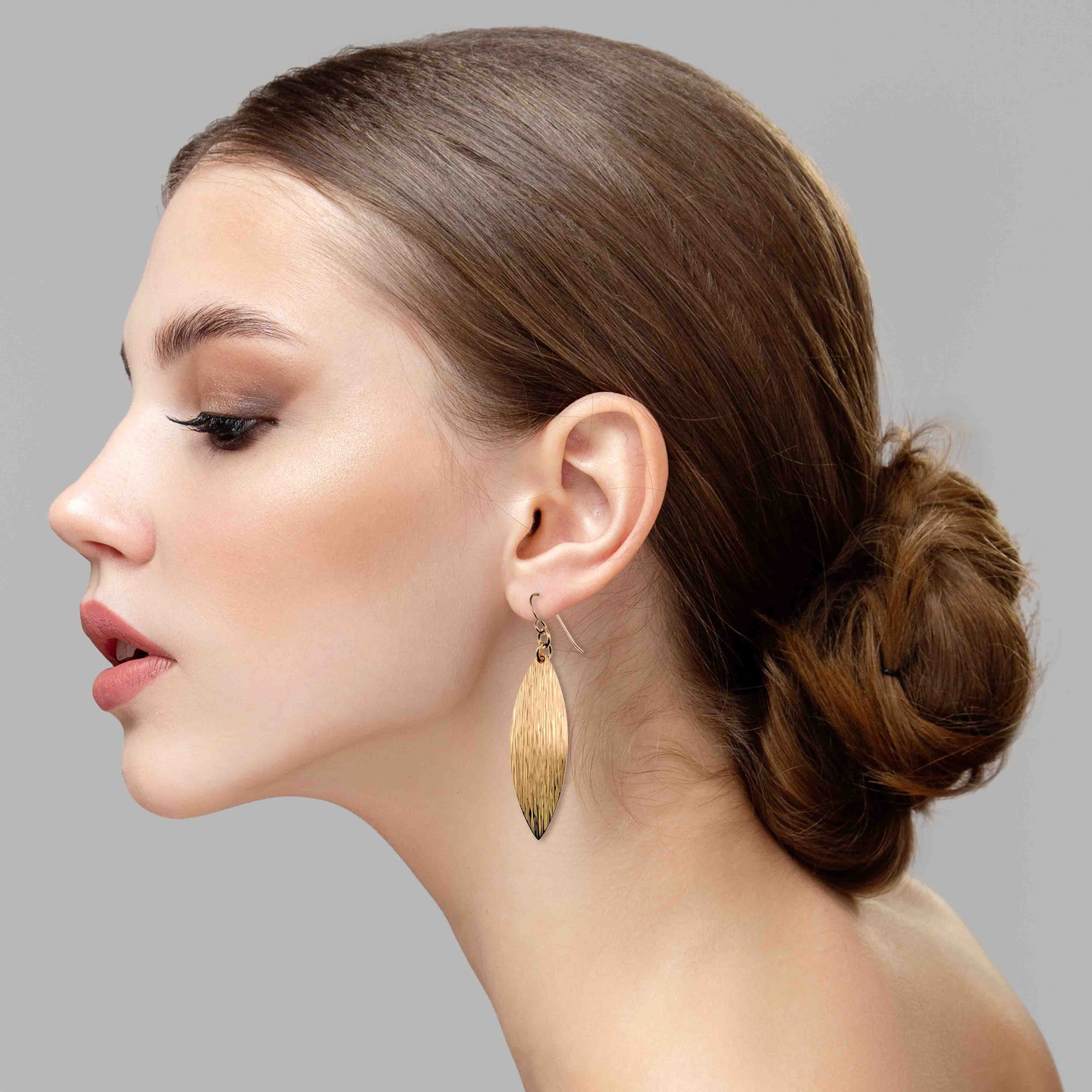 Woman wearing Bronze Bark Leaf Drop Earrings with a gray background