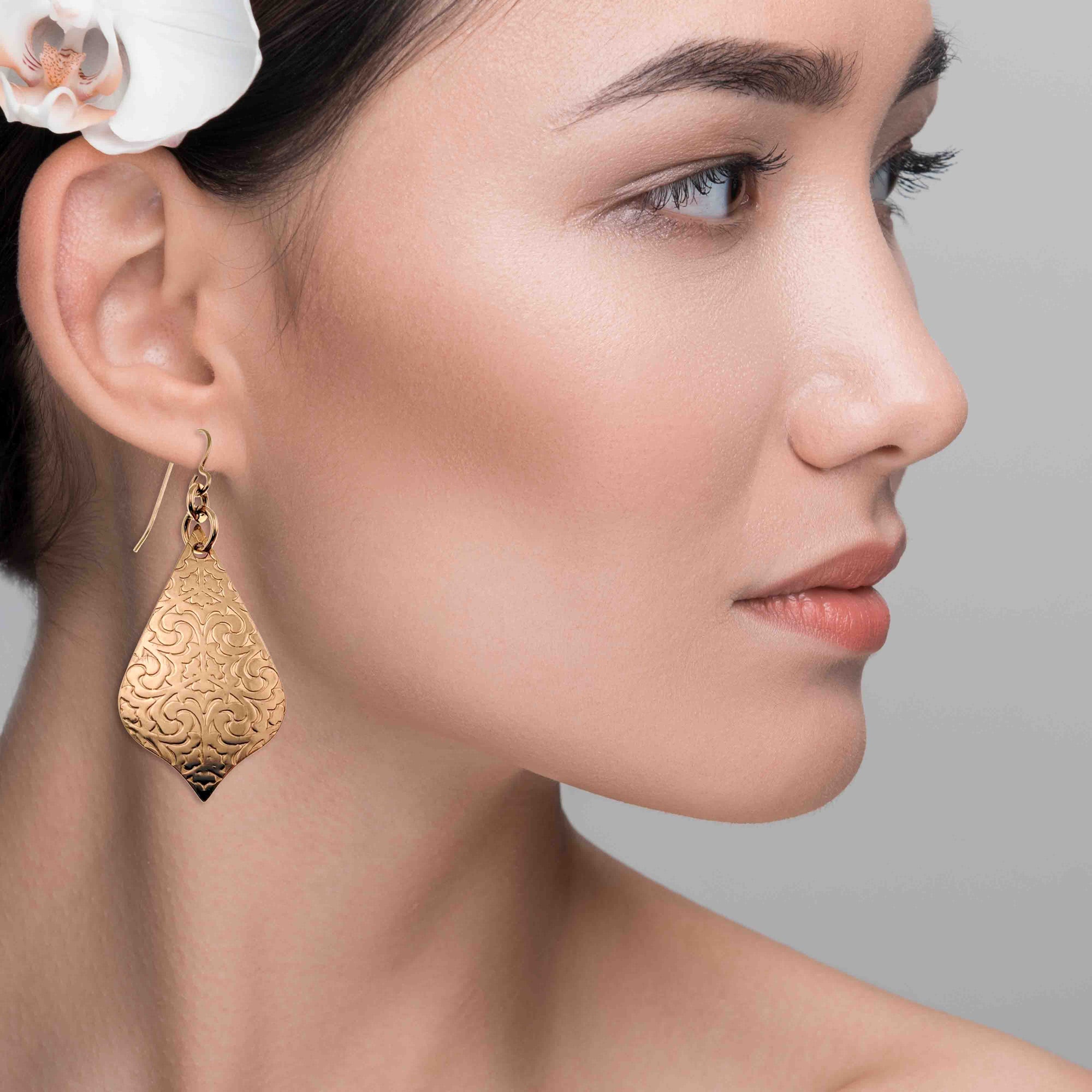 Close-up of a woman wearing Bronze Damask Arabesque Drop Earrings  with a gray background