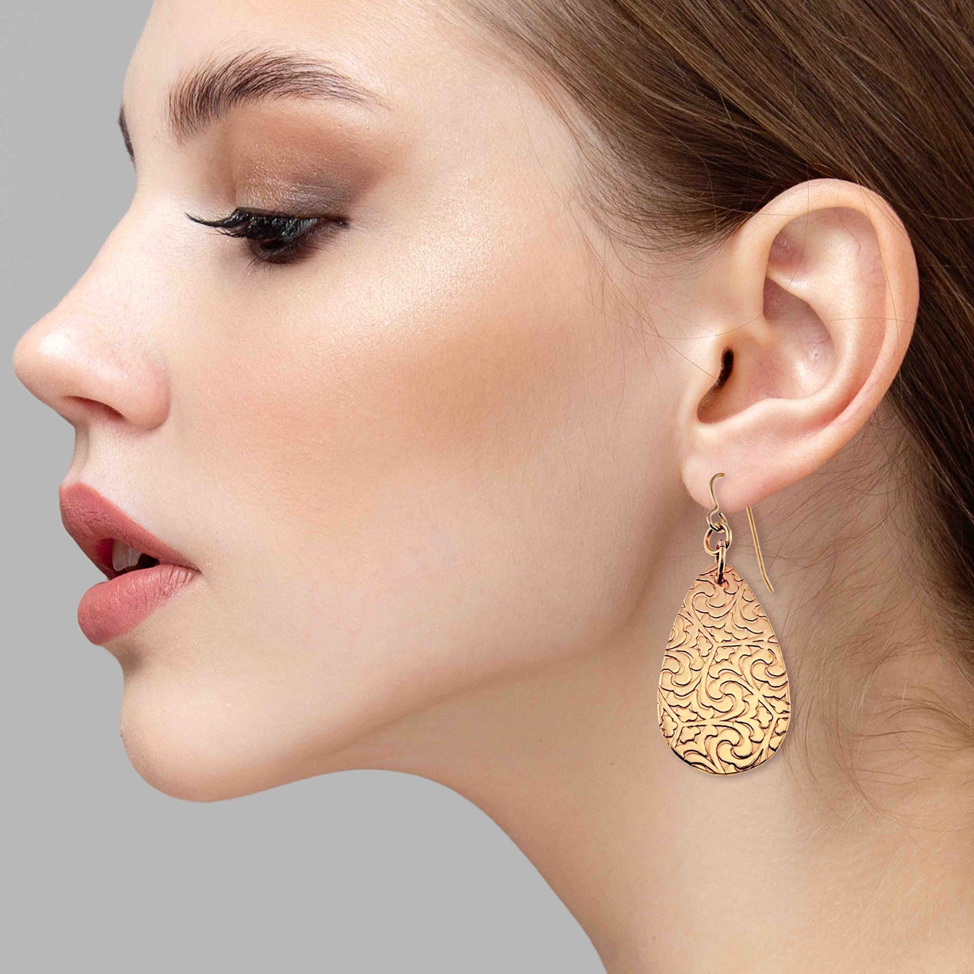 Close-up of a woman wearing Bronze Damask Teardrop Earrings against a gray background