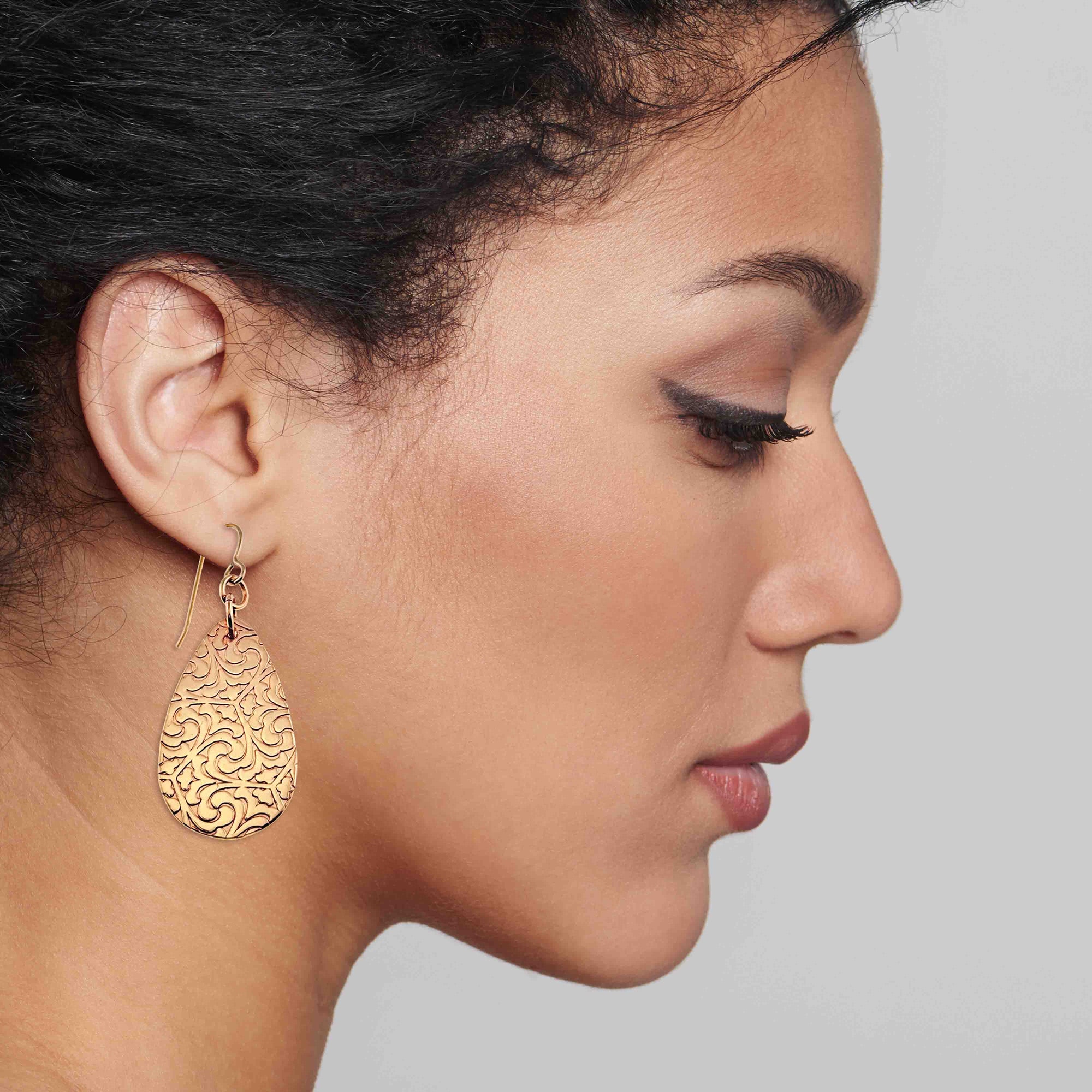 Close-up of a woman wearing Bronze Damask Teardrop Earrings against a neutral background