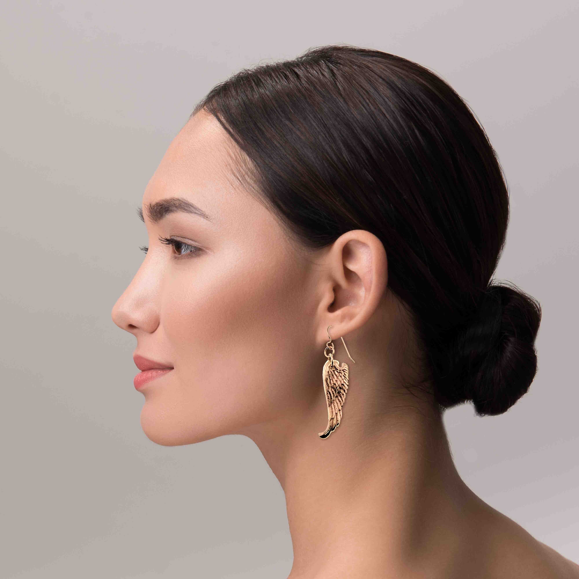 Woman wearing Bronze Guardian Angel Wing Drop Earrings against a neutral background