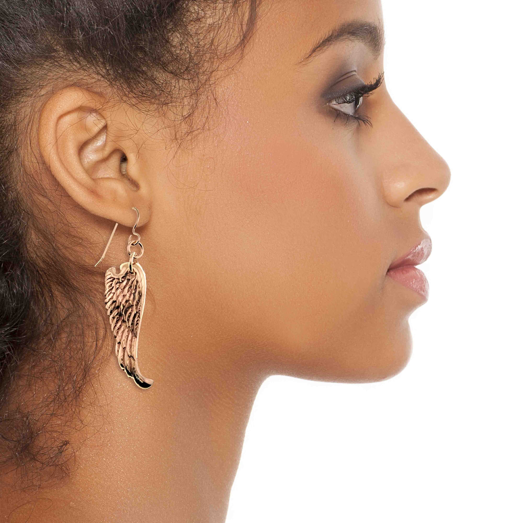 Close-up of a woman wearing Bronze Guardian Angel Wing Drop Earrings on a white background