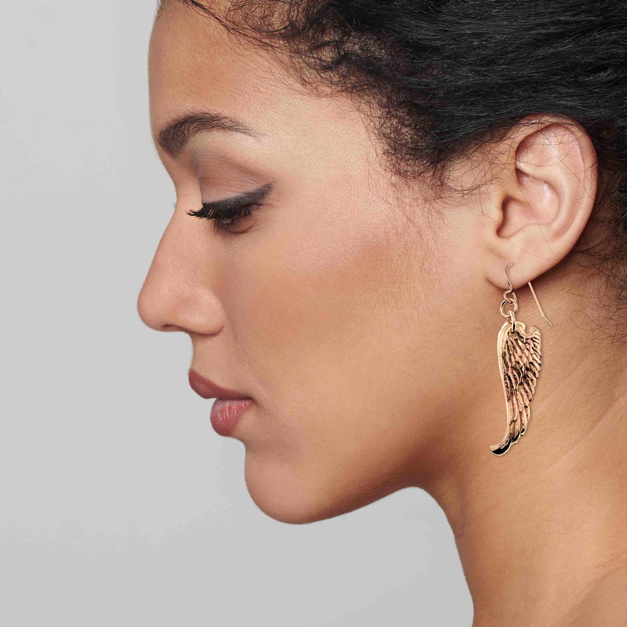 Close-up of a woman wearing Bronze Guardian Angel Wing Drop Earrings on a plain background