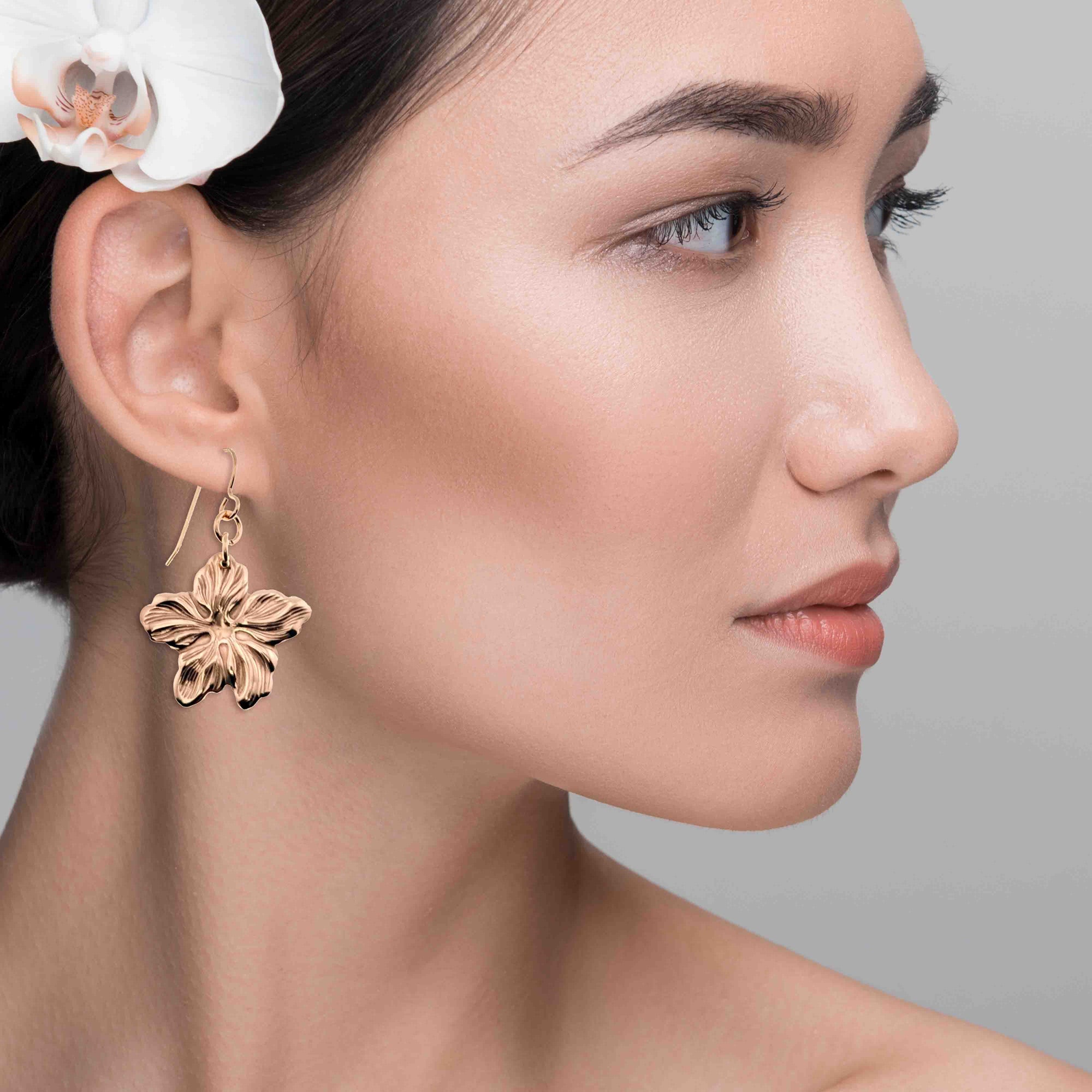 Close-up of a woman wearing Bronze Hibiscus Flower Dangle Earrings with a gray background