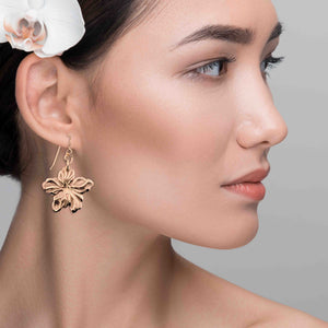 6 of 7: Close-up of a woman wearing Bronze Hibiscus Flower Dangle Earrings with a gray background