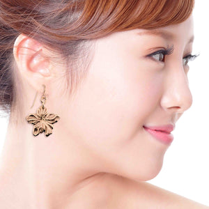 4 of 7: Close-up of a woman wearing Bronze Hibiscus Flower Dangle Earrings on a white background