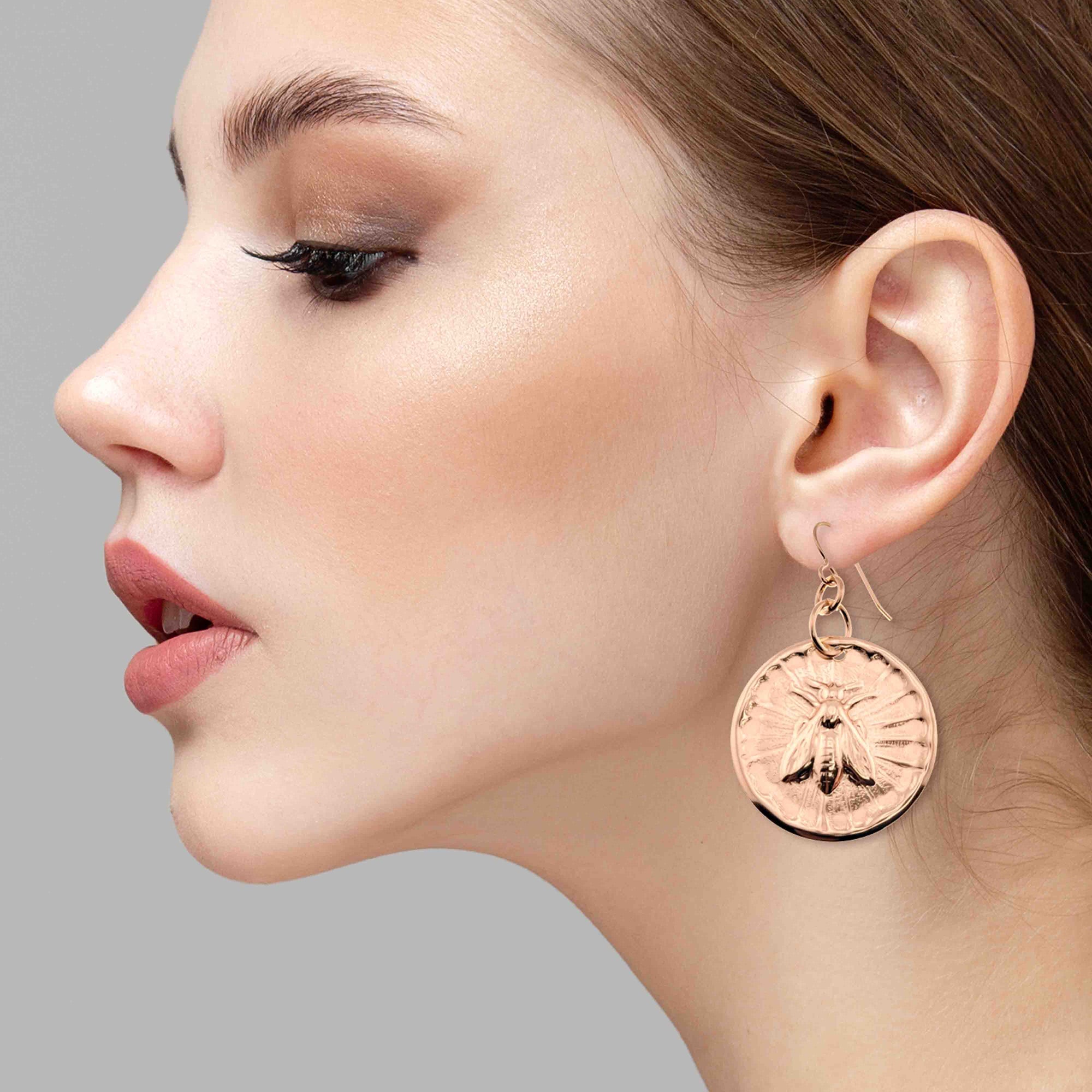 Close-up of a woman wearing Bronze Queen Bee Disc Drop Earrings against a gray background