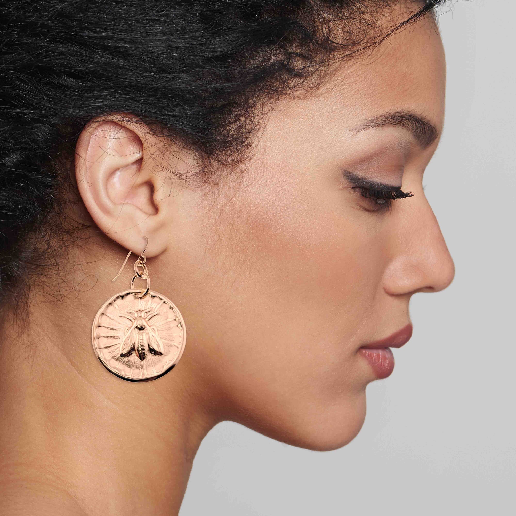 Close-up of a woman wearing Bronze Queen Bee Disc Drop Earrings with a detailed design.