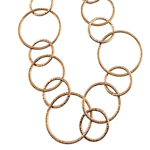 3 of 6: Close view of the Chased Bronze Link Chain Necklace showing linked bronze circles in several sizes against a white background. Hand applied chased marks run around the edges of each link, giving the polished bronze surface a textured finish that catches the light.
