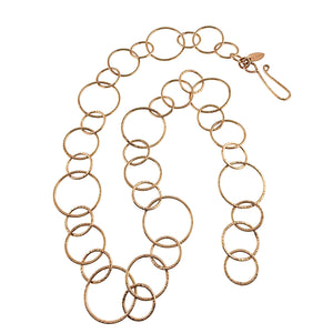 1 of 6: Full Chased Bronze Link Chain Necklace arranged in a loose curve on a white background. Varied circular and oval bronze links show the hand applied chased texture throughout the 26 inch chain. A curved hook clasp and small maker tag are visible at one end.