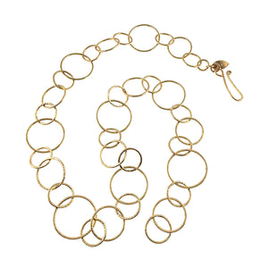1 of 8: Full view of the Chased Nu Gold Brass Chain Link Necklace arranged in a loose oval on a white background. The necklace combines large, medium, and small round and oval links with hand hammered texture, a warm golden finish, and a curved hook style clasp with a small decorative tag.