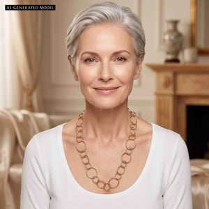 4 of 6: AI generated Woman with short silver hair wearing the Chased Bronze Link Chain Necklace with a white scoop neck top. The warm bronze necklace falls across the upper chest and features alternating circular and oval links in several sizes, with chased texture and a polished finish that stands out against the light clothing.