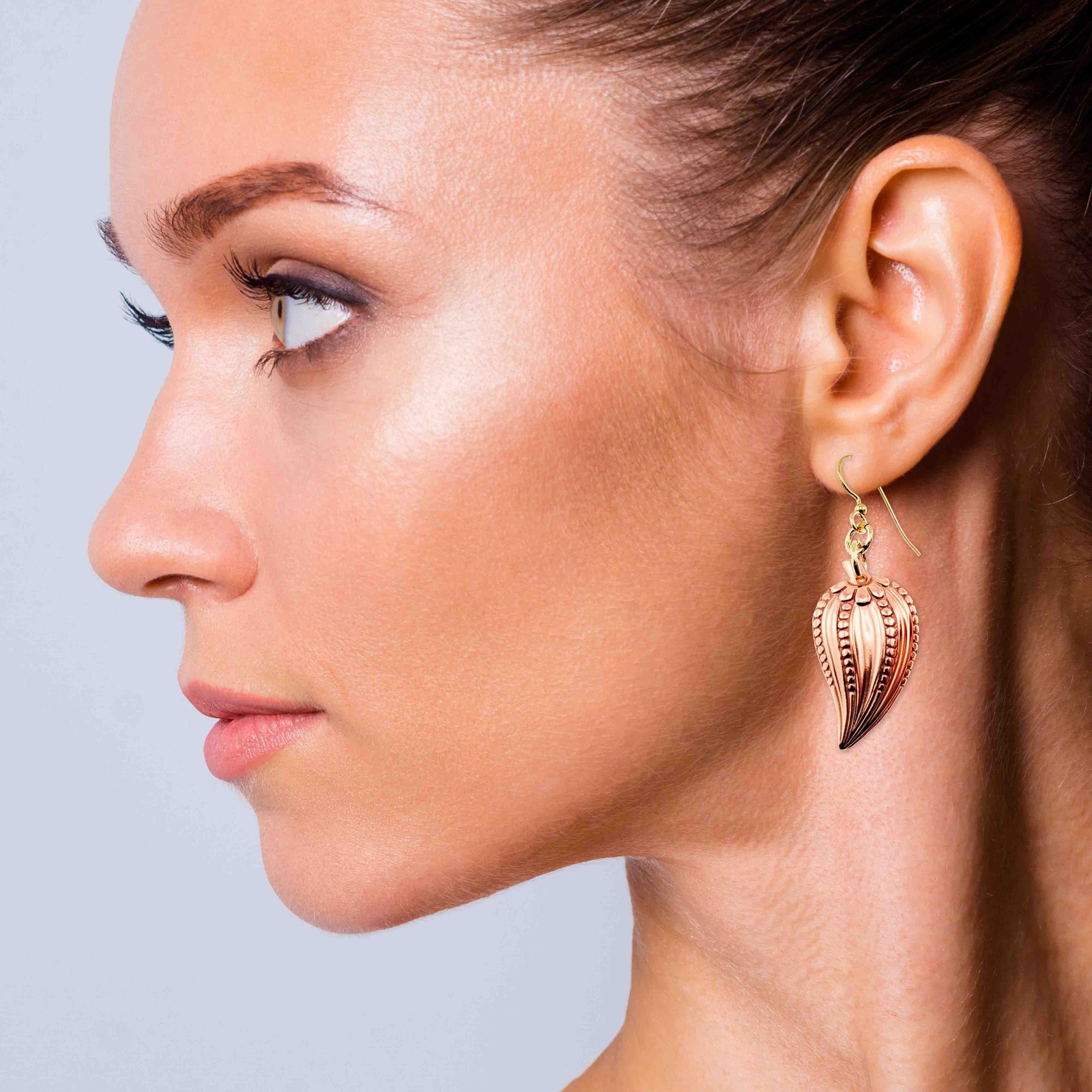 Close-up of a woman wearing Chili Pepper Copper Drop Earrings against a light blue background