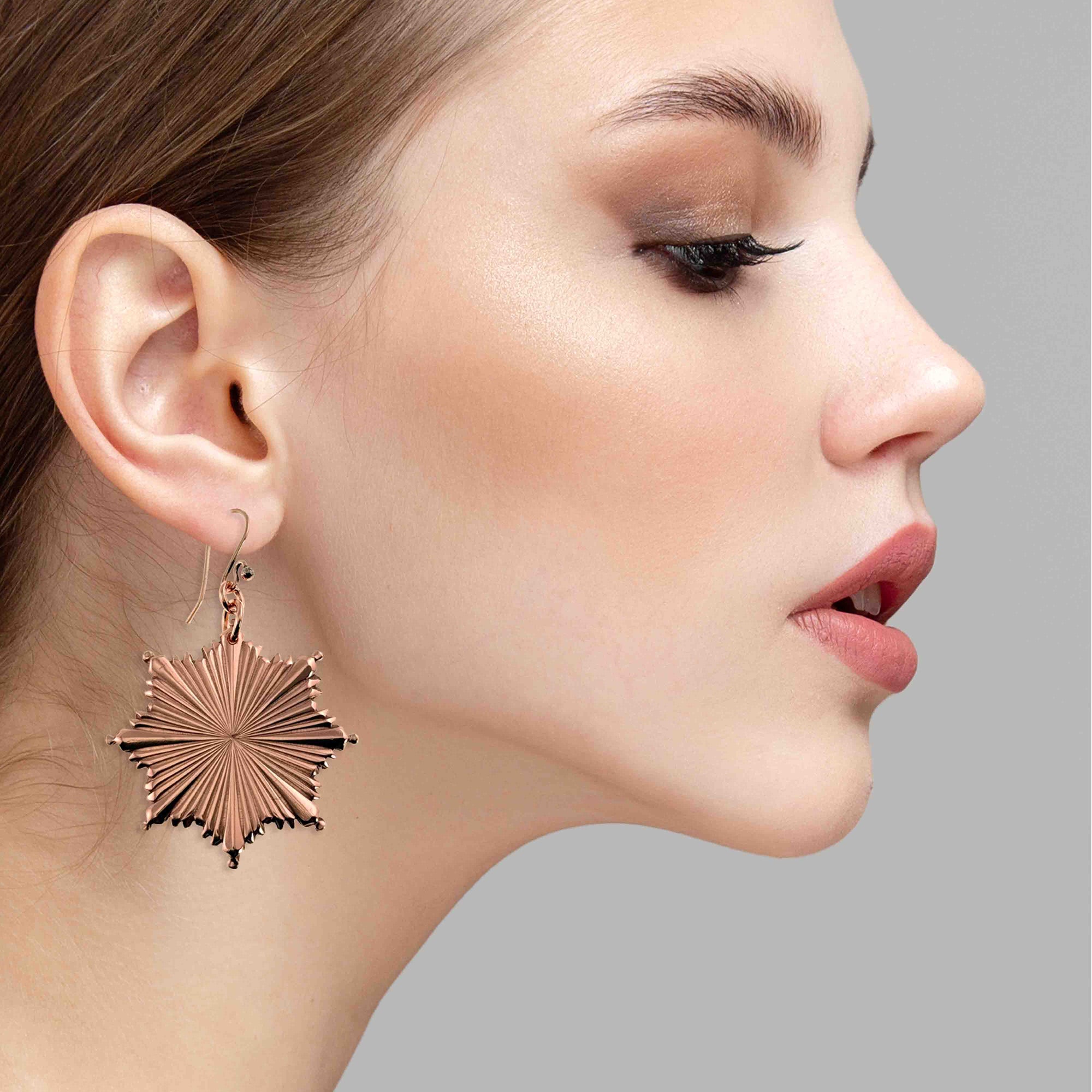 Close-up of a woman wearing a Christmas Starburst Copper Earring against a gray background