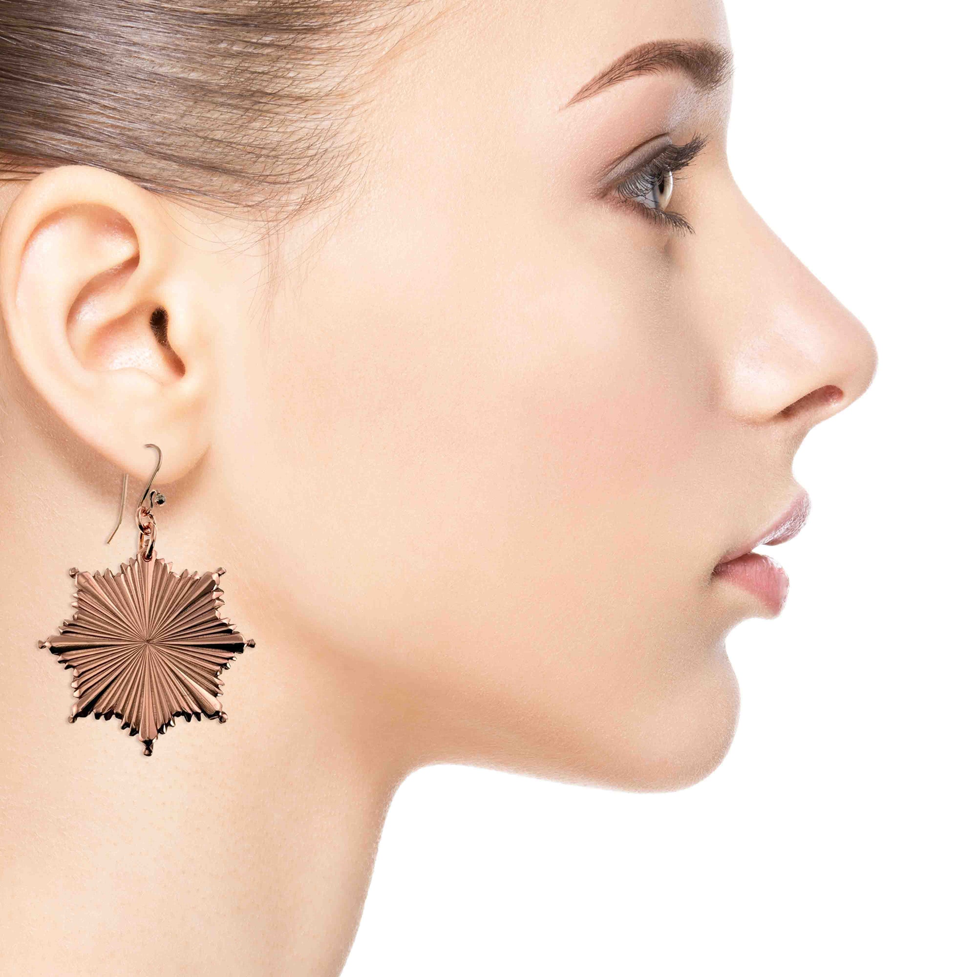 Close-up of a woman wearing a Christmas Starburst Copper Earring on a white background