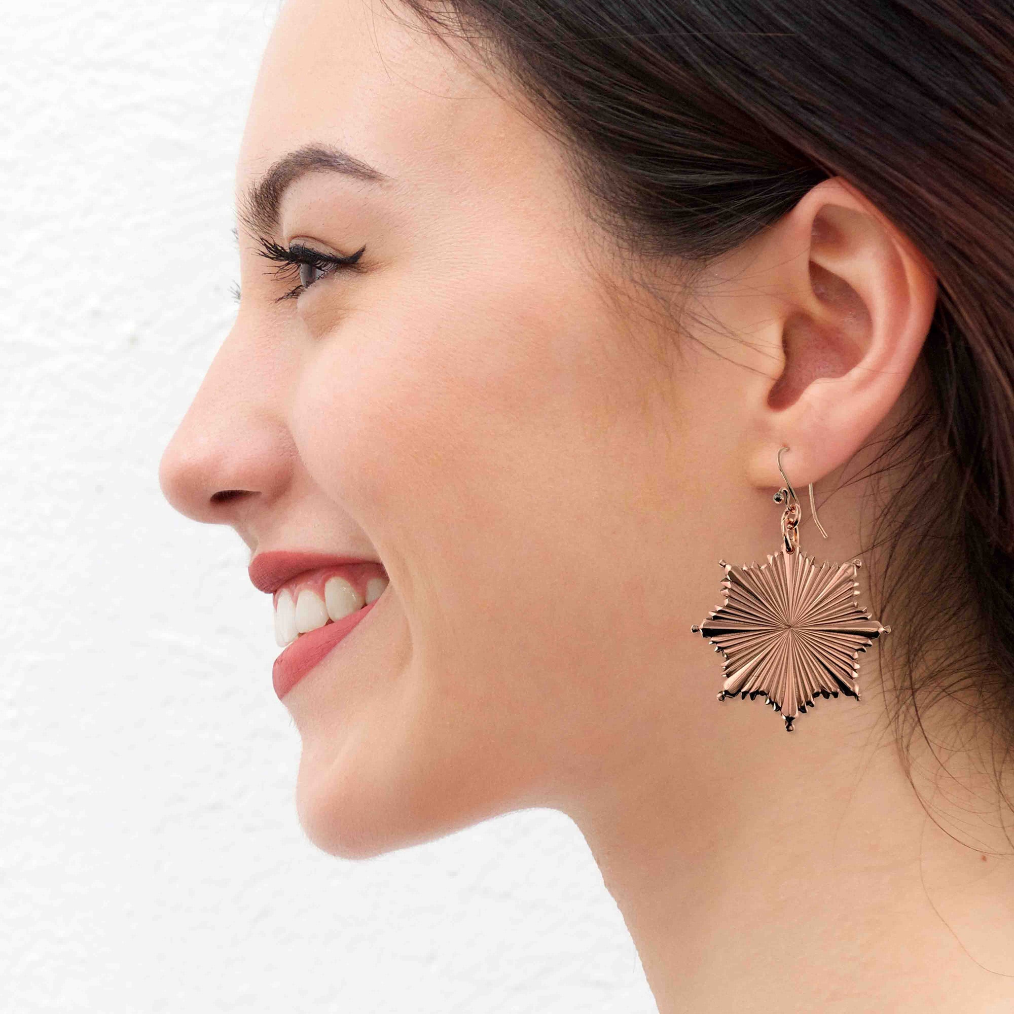 A Woman smiling while wearing a Christmas Starburst Copper Earring on a white background