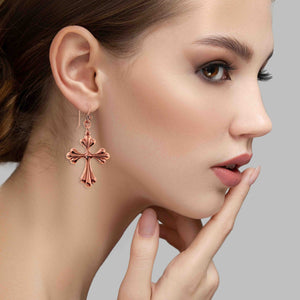 6 of 7: Close-up of a woman wearing a Copper Baroque Cross Drop Earring against a neutral background