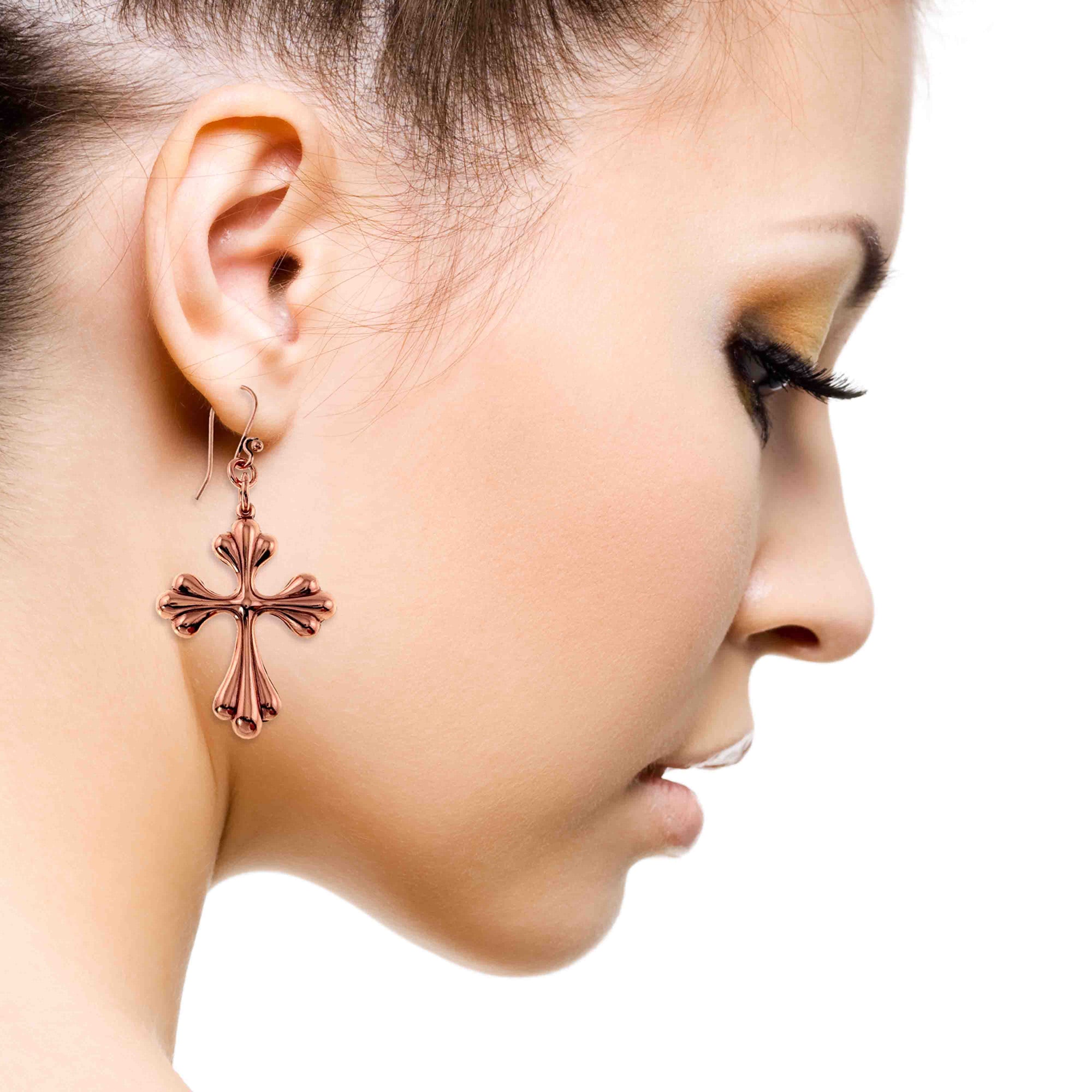 Close-up of a woman wearing a Copper Baroque Cross Drop Earring on a white background
