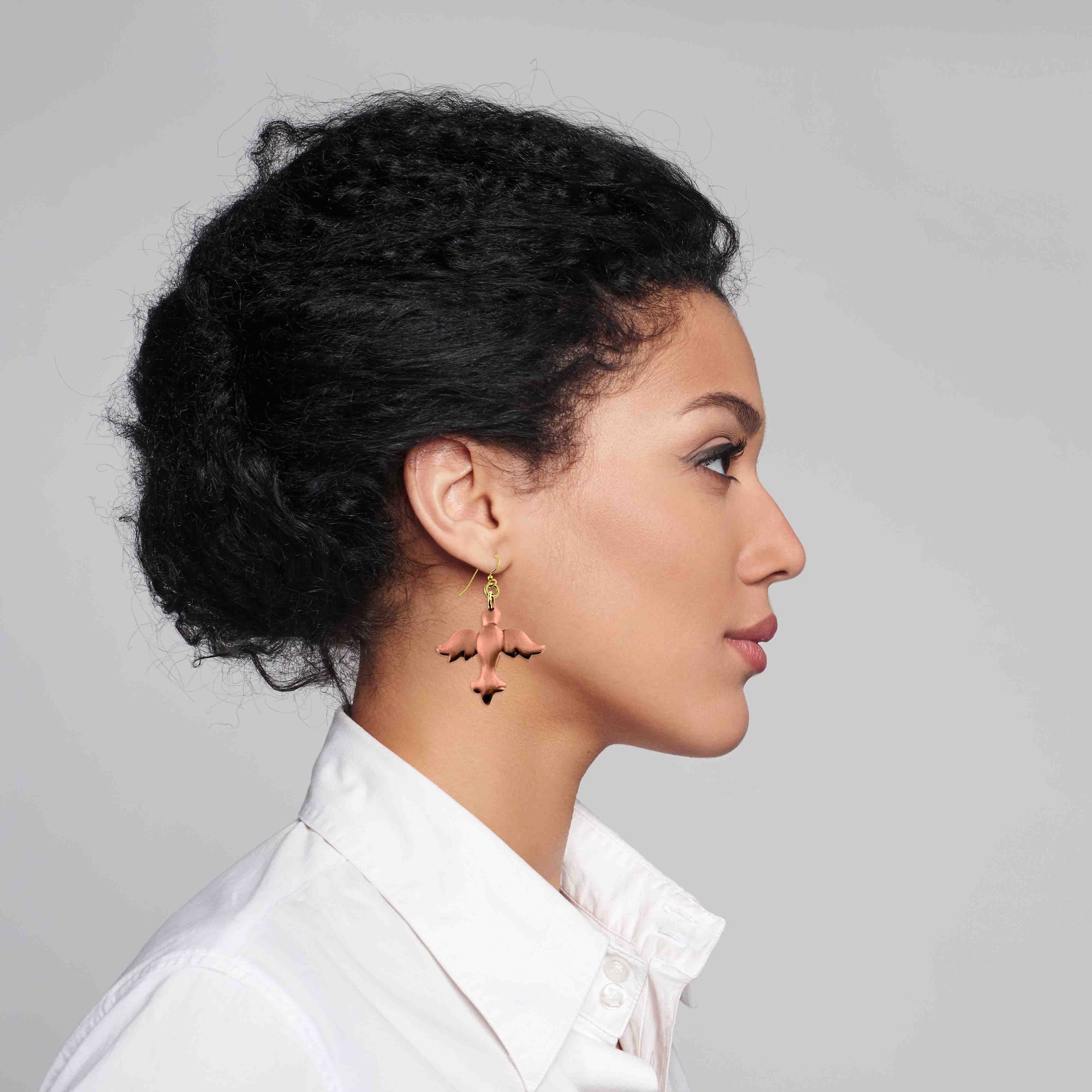 Woman with styled hair wearing Copper Christmas Dove Dangle Earrings with a white shirt against a gray background