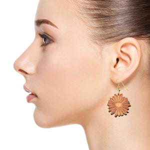 4 of 7: Side profile of a woman wearing a handcrafted copper daisy dangle earring with detailed petal texture and a polished finish. The earring hangs from a gold tone brass French hook, showing its size and how it rests just below the earlobe, catching the light with a warm glow against her skin.