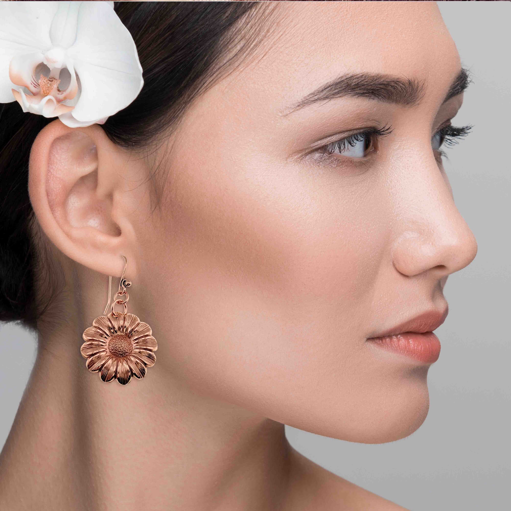 Close-up of a woman wearing Copper Daisy Disc Drop Earrings  with a white orchid in her hair.