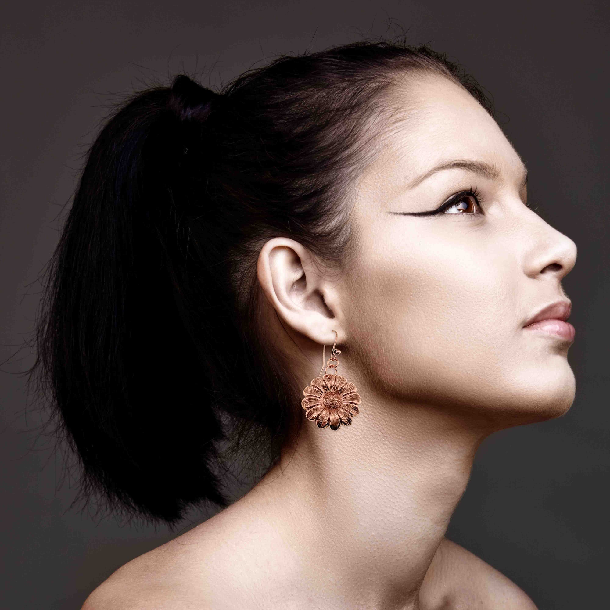 Woman wearing Copper Daisy Disc Drop Earrings against a dark background