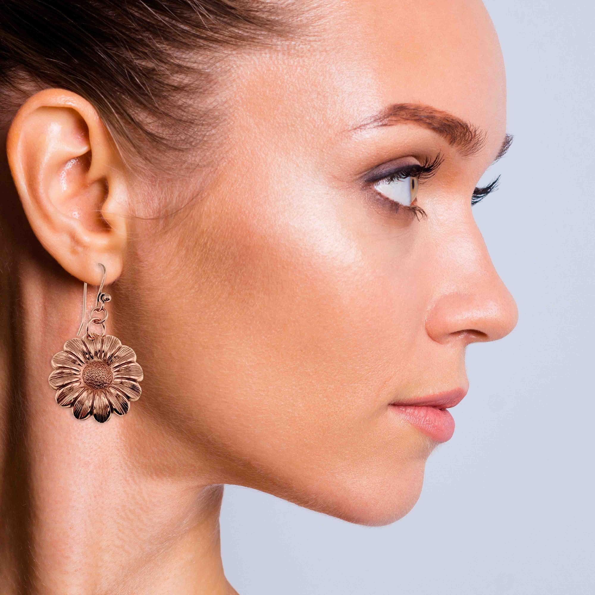 Close-up of a woman wearing Copper Daisy Disc Drop Earrings  against a neutral background