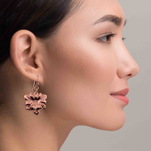 6 of 7: Close-up of a woman wearing Dogwood Blossom Copper Drop Earrings against a neutral background