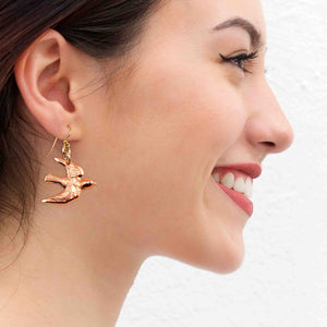 2 of 7: A Smiling Woman Wearing Copper Flying Swallow Earrings
