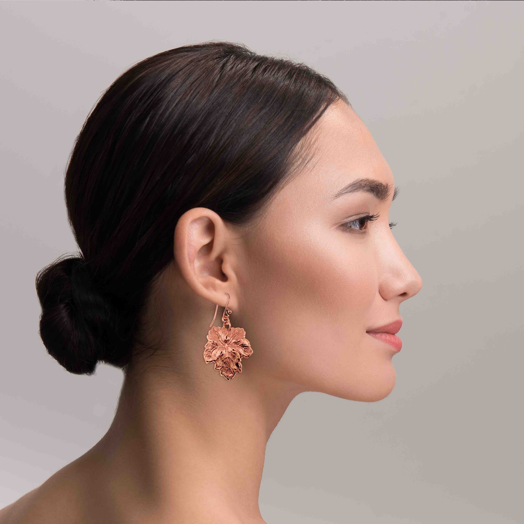 Woman wearing Grape Leaf Copper Dangle Earrings with a plain background